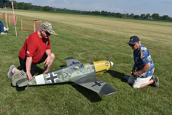 Two men kneeling on grass with a large model airplane.