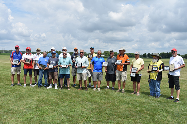 Group of people standing on grass holding plaques under a cloudy sky.