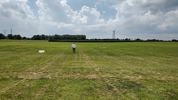 Man walking across a vast, green field under a partly cloudy sky.