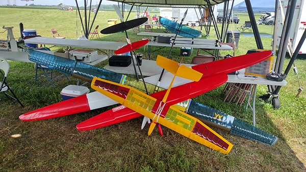 Model airplanes with colorful wings displayed on a table under a tent.
