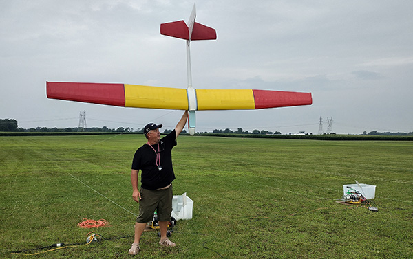 Man holding a large model airplane in a grassy field.