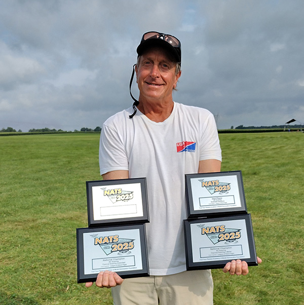 Man smiling, holding four framed awards in a grassy field.