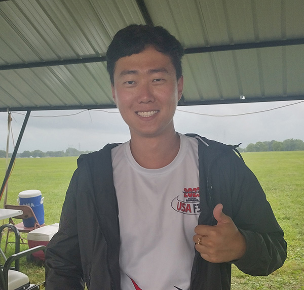 Smiling person under a metal canopy, thumbs up.