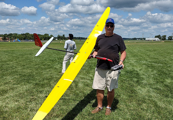 Person holding a large yellow glider on a grassy field under a cloudy sky.