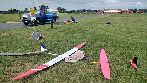 Model airplanes on grass near parked truck and people.