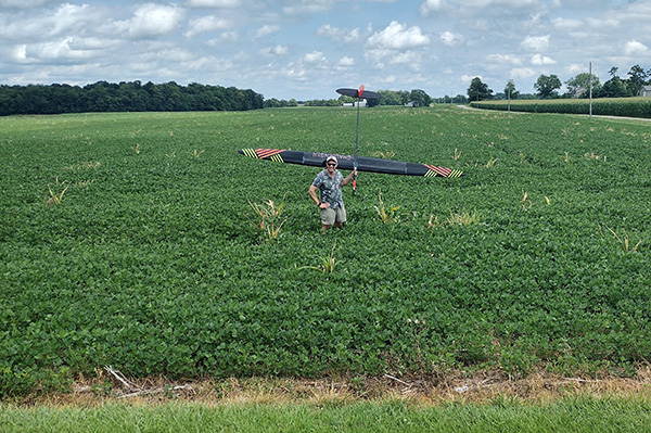 Man standing in a green field with a large drone above him.