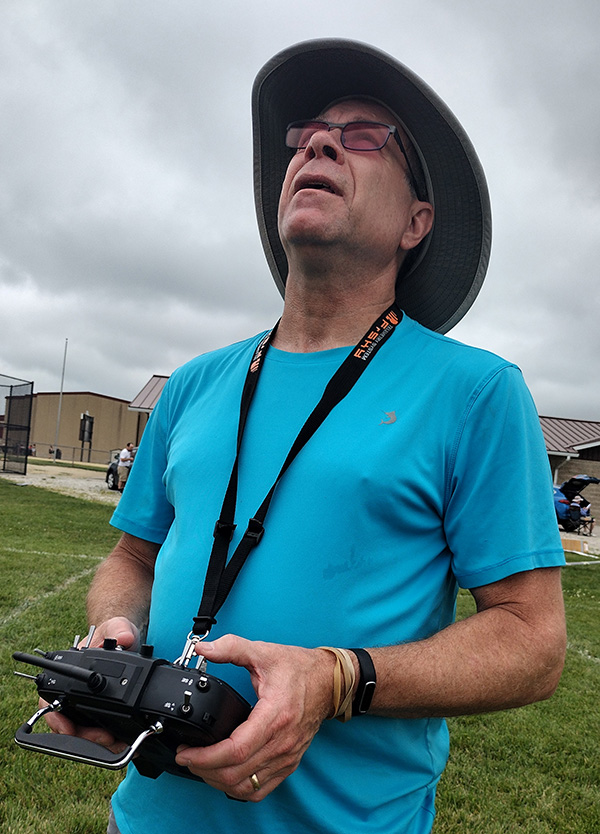 Man in a blue shirt wears a wide-brim hat, holding a device while looking up.