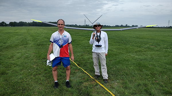 Two men on a grassy field with a glider in the background.