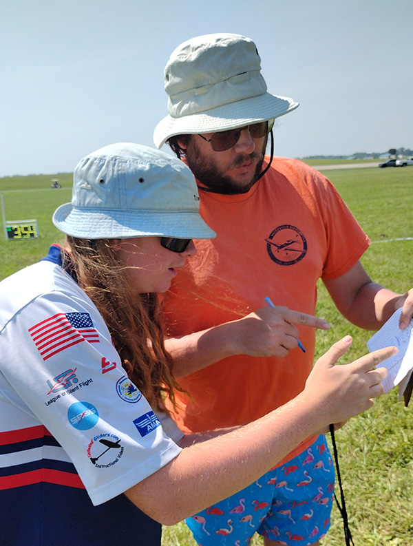 Two people in hats outdoors, discussing notes.