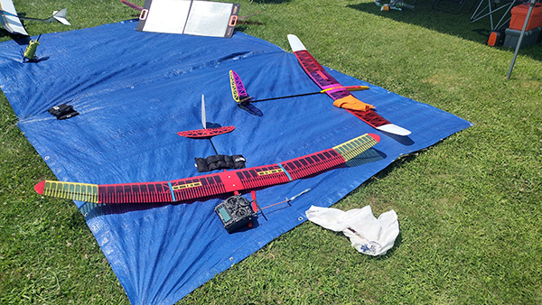 Remote-controlled gliders on a blue tarp, grass in background.