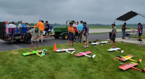 Remote-controlled planes and people on grass at an outdoor field.