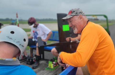 Group preparing for kart racing on a cloudy day, wearing helmets and colorful attire.