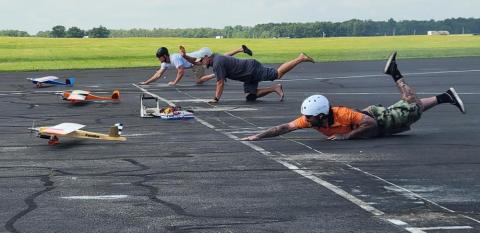 Three people with toy planes, pretending to fly, lying on a runway.
