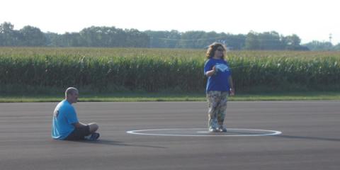Man sitting and another standing on an asphalt road near a cornfield.