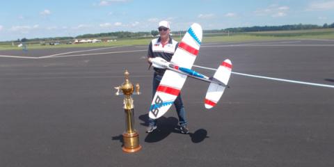 Man with model airplane, standing beside large trophy on airfield.
