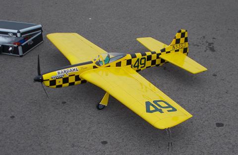 Yellow model plane with checkered black details and a propeller, on a gray surface.