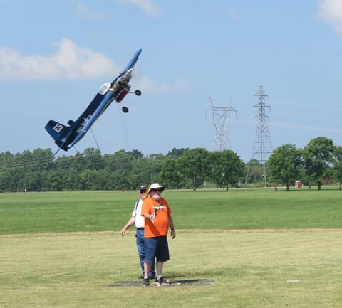 Remote-controlled plane flies low over a grassy field with power lines in the background.