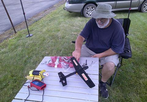 Man assembling model airplane outdoors on a table.