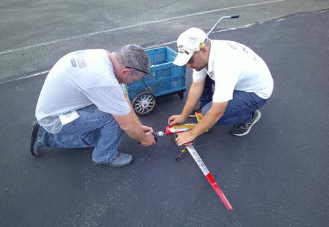Two men kneeling, assembling a small model airplane on pavement.
