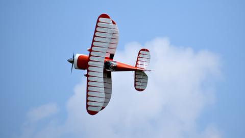 Red biplane flying against a blue sky with white clouds.
