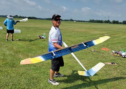 Man holding a large model airplane in a grassy field.