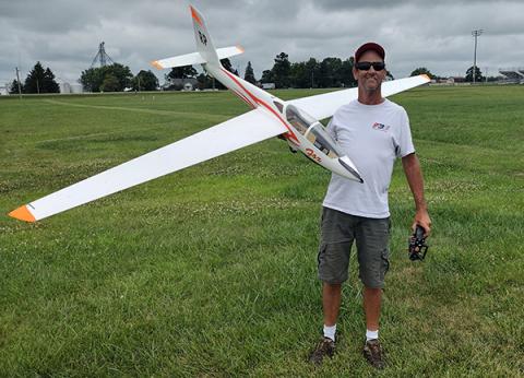 Man holding a large model airplane on a grassy field.