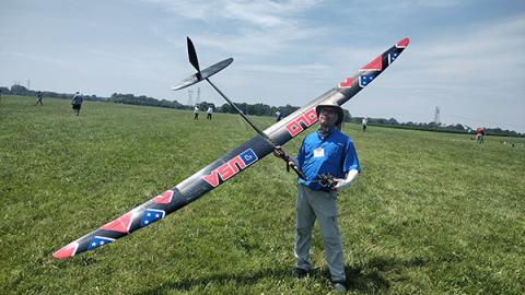 Man holding large model glider on grassy field under blue sky.