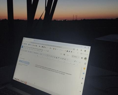 Laptop screen displaying a document, set against a dimly lit, post-sunset sky.