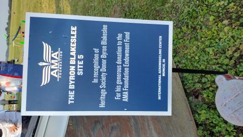 Sign honoring donor Byron Blakeslee at an aeromodeling center, grass in the background.