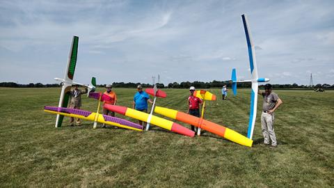 Five people holding colorful model gliders on a grassy field.