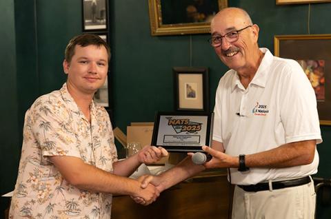 Two people shaking hands, one holding a 2023 award plaque, both smiling.