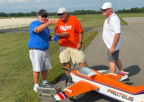 Three men laughing near a model airplane on a runway.