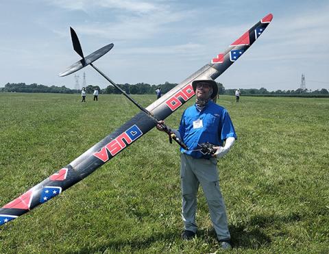 Man holding large model glider on grassy field.