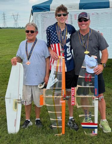 Three men with medals holding remote-controlled airplanes, standing on grass.