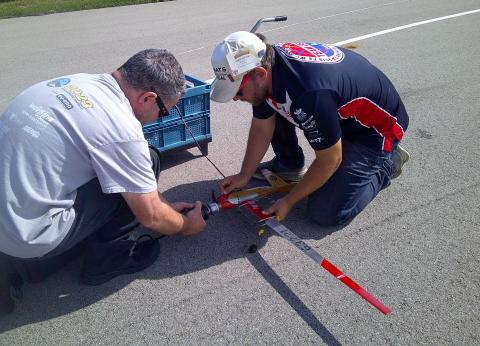 Two men adjusting a red model airplane on a paved surface.