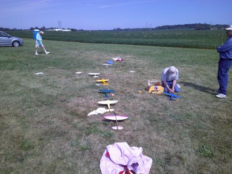 Model airplanes on grass, two people with them, clear sky.