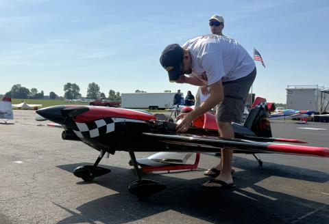 Man inspecting a model airplane on a sunny tarmac; another man stands nearby.