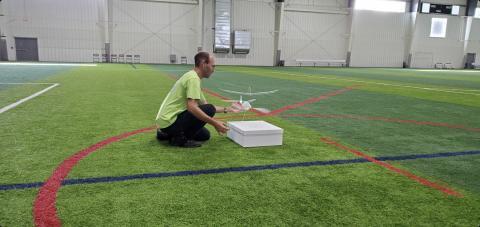 Man kneeling on indoor field with drone and box.