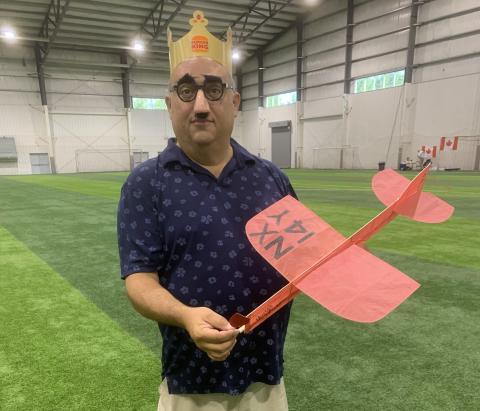Man in crown holds a red model plane in an indoor sports facility.