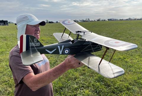 Man holding a green model biplane in a grassy field.