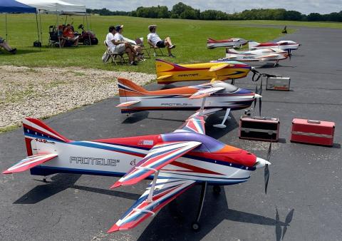 Toy airplanes lined up outdoors, people sitting under canopies in background.