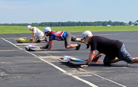 Four people on knees racing small model airplanes on a paved track.