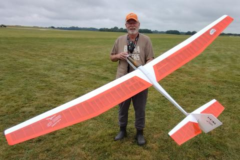Man happily holding a large, orange remote-controlled glider on a grassy field.