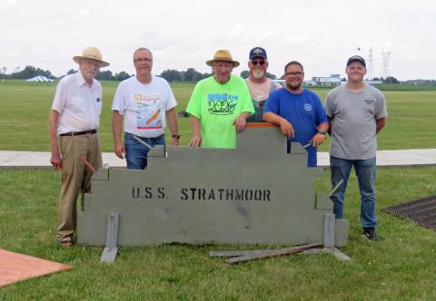 Five men standing behind a USS Strathmoor sign on a grassy field.