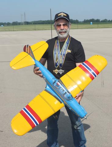 Man holding a yellow and blue model airplane on an airstrip.