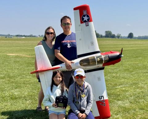 Family smiling with a large model airplane on a grassy field.