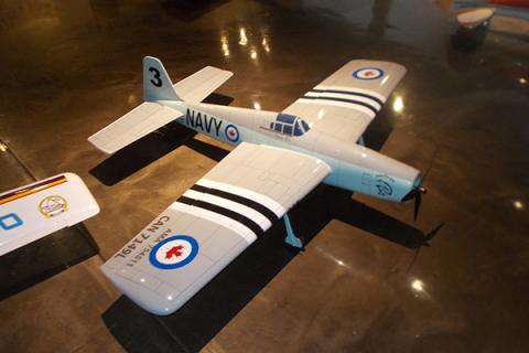 Model airplane with silver body, black stripes, and navy markings on a reflective floor.