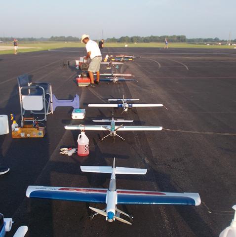 Model aircraft lined up on a runway, person adjusting controls nearby.