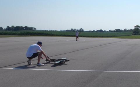 Two people preparing a model aircraft on a wide, open runway.