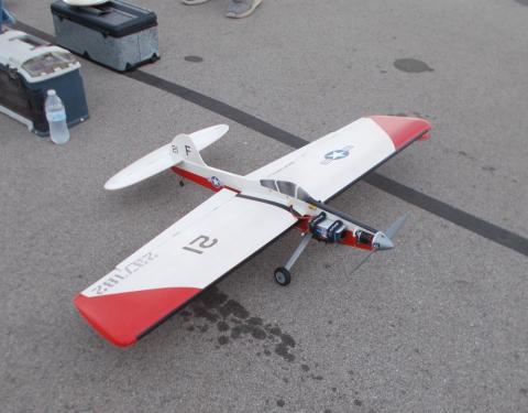 Remote-controlled airplane on pavement with red and white design.